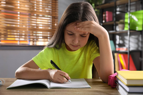 Emotional preteen girl doing homework at table - Zdjęcie, obraz