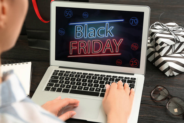 Woman using laptop with Black Friday announcement at wooden table, closeup - Foto, Imagem