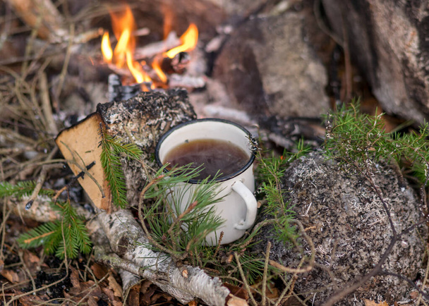 taza de metal con té se calienta junto al fuego, tiempo de otoño, la quema de leña, ramas y humo, tiempo de otoño - Foto, Imagen