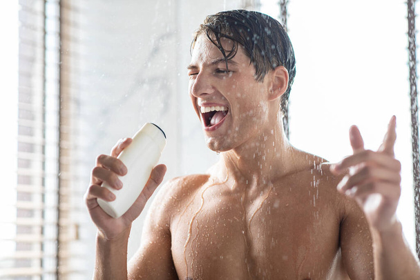 Jeune homme lavant le corps chantant dans une bouteille de shampooing - Photo, image
