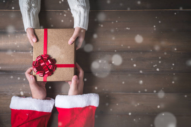 Маленькие руки Санта-Креста дарят подарки детям на Рождество. фон из дерева и снега с копировальным пространством. - Фото, изображение