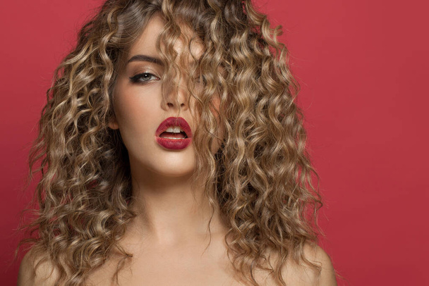 Fashion portrait of perfect model woman with makeup and curly hairstyle on red background - Fotó, kép