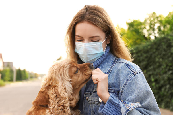 Woman in protective mask with English Cocker Spaniel outdoors. Walking dog during COVID-19 pandemic - Photo, image