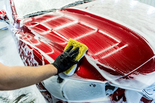 Worker washing red car with sponge on a car wash - Фото, изображение