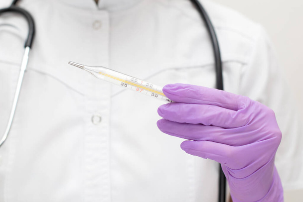 Les médecins remettent des gants médicaux tenant un thermomètre au mercure. Infirmière en uniforme avec stéthoscope mesure la température - Photo, image