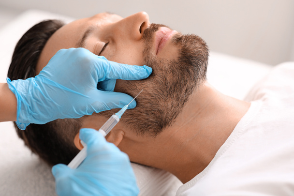 Косметолог проводит антивозрастную процедуру для красивого мужчины в клинике - Фото, изображение