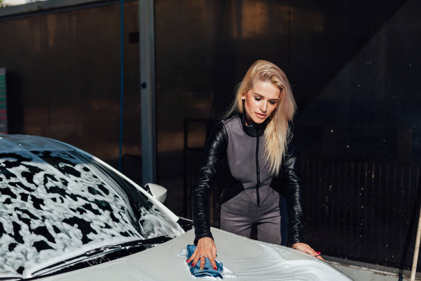 Beautiful blonde woman washes her car at car wash - Foto, afbeelding