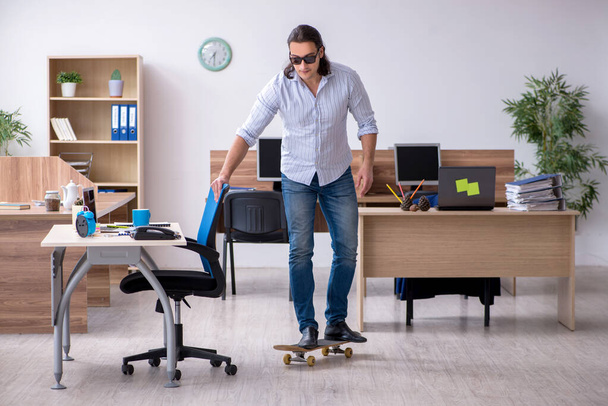 Jeune employé masculin avec skateboard dans le bureau - Photo, image