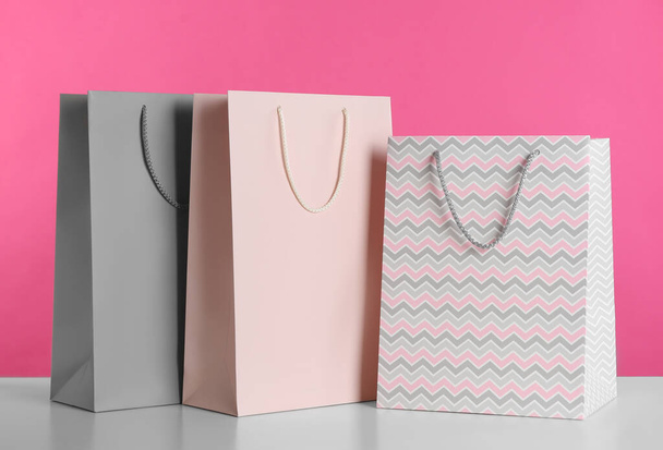 Gift bags on white table against pink background - Фото, зображення