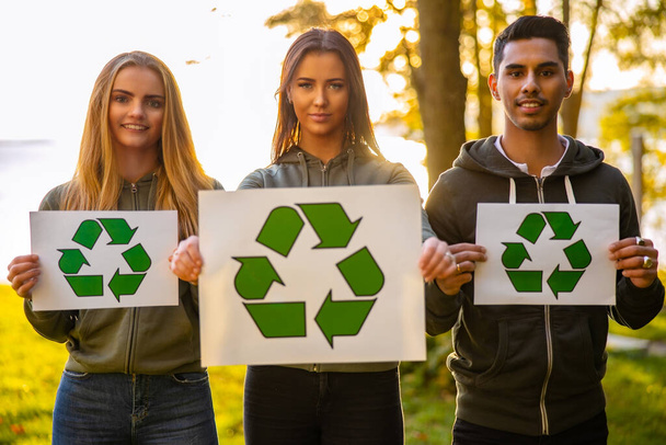 Jóvenes voluntarios protectores del medio ambiente sosteniendo cartel de símbolo de reciclaje - Foto, imagen