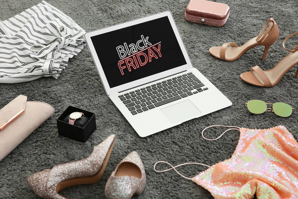 Laptop with Black Friday announcement surrounded by clothes and accessories on grey carpet - Foto, afbeelding
