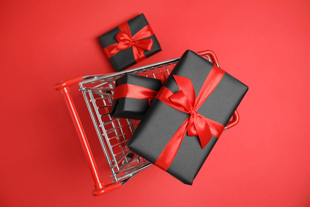 Small shopping cart with wrapped gift boxes on red background, top view. Black Friday sale - Foto, Imagem