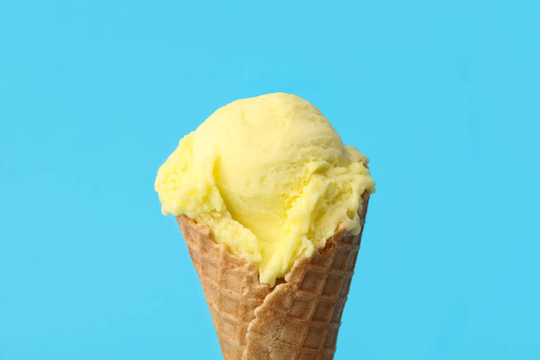 Delicious yellow ice cream in waffle cone on light blue background, closeup - Fotoğraf, Görsel