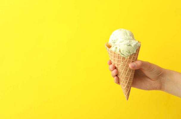 Woman holding waffle cone with delicious ice cream on yellow background, closeup. Space for text - Photo, Image