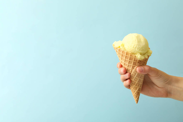 Woman holding waffle cone with delicious yellow ice cream on light blue background, closeup. Space for text - Valokuva, kuva