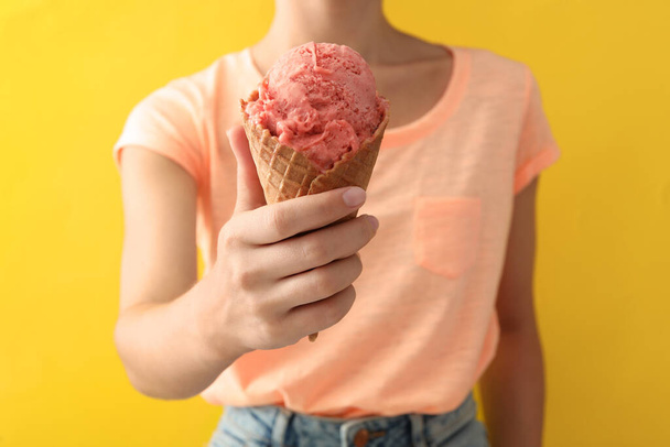 Woman holding pink ice cream in wafer cone on yellow background, closeup - Photo, image