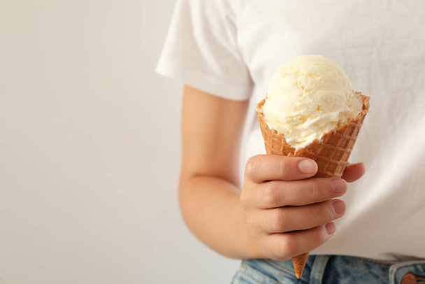 Woman holding ice cream in wafer cone on light background, closeup. Space for text - Valokuva, kuva
