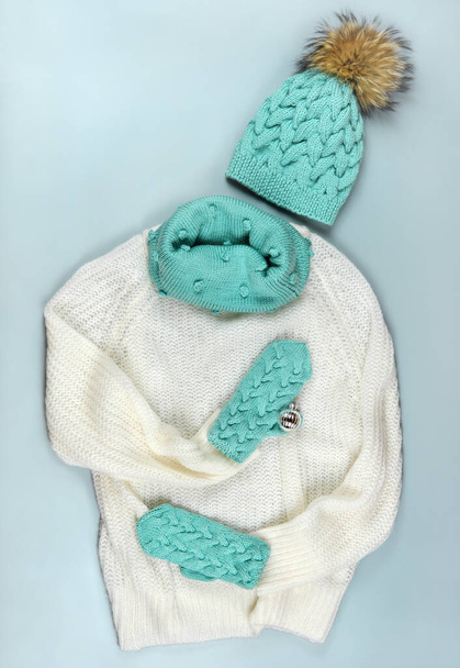 білий светр з бірюзовим капелюхом, шарфом і рукавичками. святковий зимовий модний одяг колаж на сірому фоні. вид зверху. плоский ліжко
. - Фото, зображення