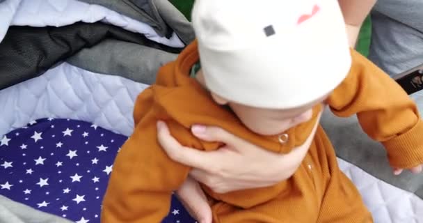 Primo piano delle mani della madre, mettere amorevolmente il suo piccolo bambino carino in un passeggino - Filmati, video