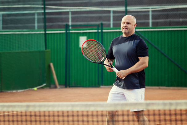 An aged man plays tennis on the court. Active lifestyle and health. - Photo, Image