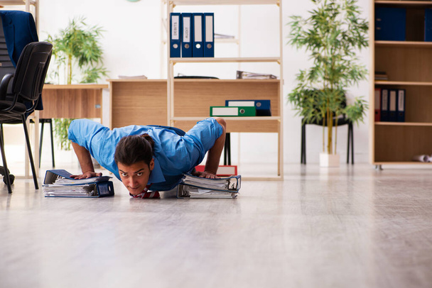 Young male employee doing sport exercises at workplace - Photo, Image