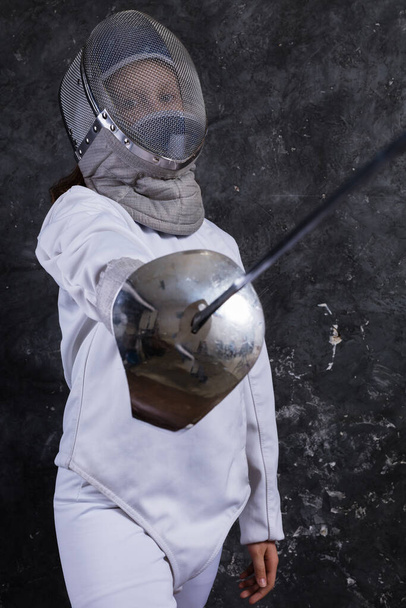 Teenage girl fencer dressed in uniform with epee and helmet - Φωτογραφία, εικόνα