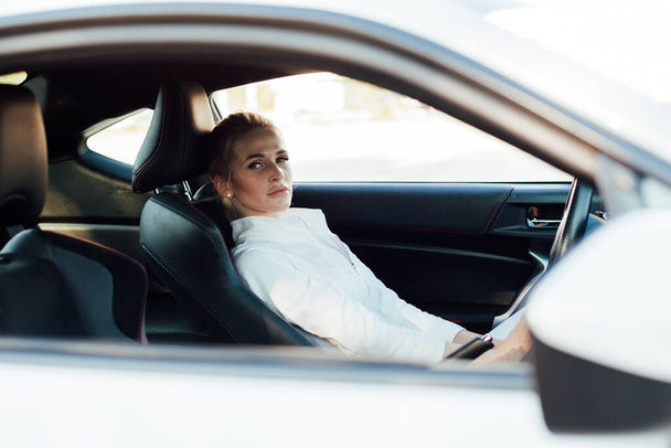 Mooie vrouwelijke blonde bestuurder achter het stuur van een auto op de weg - Foto, afbeelding