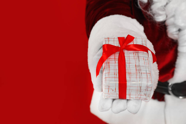 Santa Claus holding Christmas gift on red background, closeup. Space for text - 写真・画像