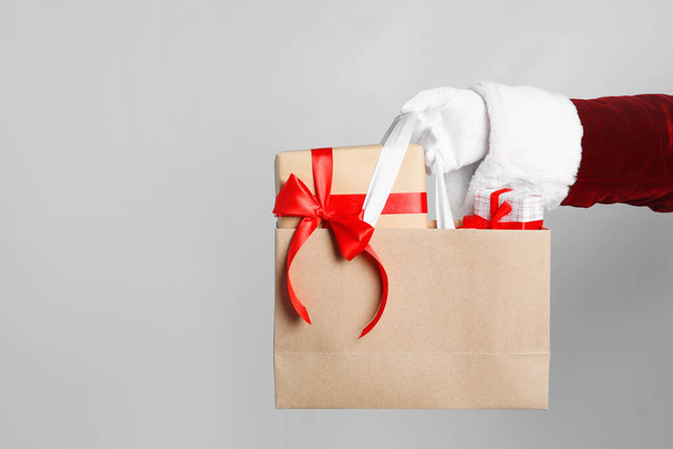 Santa holding paper bag with gift boxes on light grey background, closeup - Zdjęcie, obraz