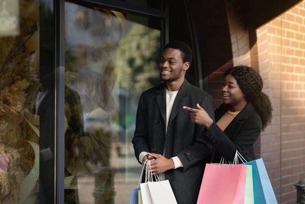 Cooler Verkauf im Markenladen, ich will ihn. Interessante afrikanisch-amerikanische Kerl und Dame mit farbigen Papiertüten zu Fuß auf die Straße - Foto, Bild