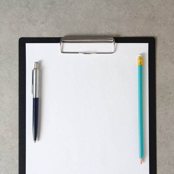 Template of white paper with a ballpoint pen and simple pencil on light grey concrete background in a black tablet with a clip. Concept of new idea, business plan and strategy, development and implementation of content. Stock photo with empty space f - Fotoğraf, Görsel