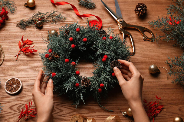 Florist making beautiful Christmas wreath with berries and pine cones at wooden table, above view - Photo, image