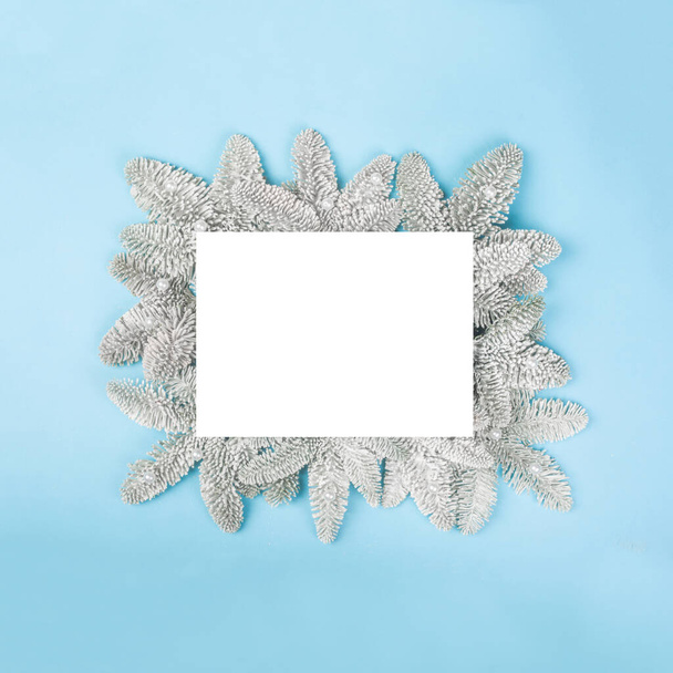 Frosted fir tree twigs and Christmas decorative snowflakes on blue background with white card with copy space for text template flat lay top view design - Photo, image