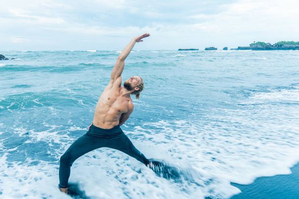 Athlete man practicing on a beach shore with waves coming in - Фото, зображення