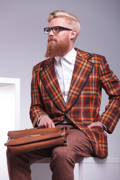 Lado de un modelo masculino de moda sentado sosteniendo su maletín
 - Foto, imagen