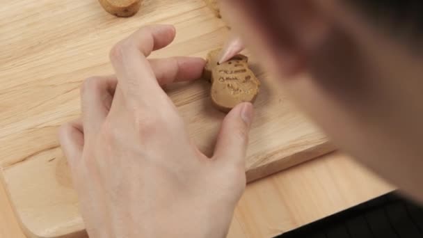 Zbliżenie kucharz podnoszenie i wyciskanie śmietany cukrowej na Boże Narodzenie domowej roboty pierniki bałwan ciasteczka na drewnianej tacy - Materiał filmowy, wideo