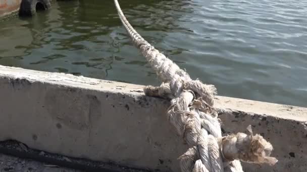 Mooring rope against background of water in port on river, lake, ocean, sea. Against the background of concrete quay wall and car wheels, fender - Footage, Video