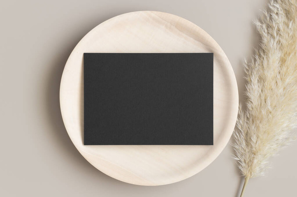Запрошення чорної листівки макет на дерев'яній тарілці з травою пампушок. 5x7 співвідношення, подібне до A6, A5
. - Фото, зображення
