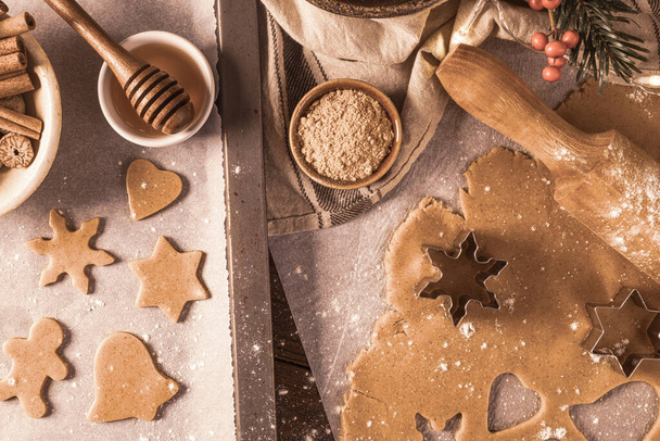 Making christmas gingerbread cookies. Raw dough in shape of gingerbread man, christmas tree, star, snowflakes on paper on tray on rustic table with rolling pin. Preparing for baking - Zdjęcie, obraz