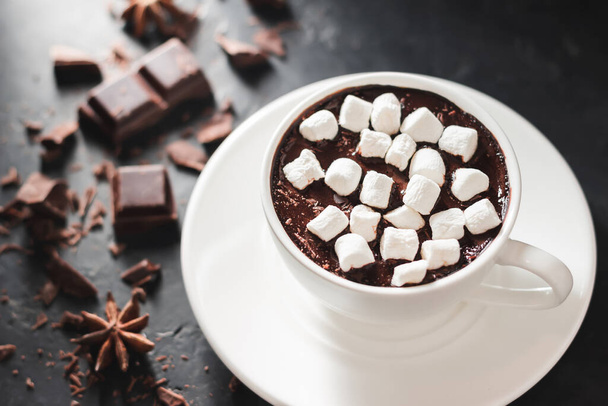 Heißes Schokoladengetränk in weißer Tasse mit Eibisch, gebrochenen Schokoladenwürfeln und Sternanis auf dunklem Hintergrund. - Foto, Bild