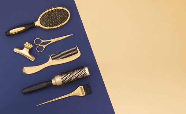 Hairdressing tools on a blue background and a yellow sheet with space for text. Gold hair salon accessories, comb, scissors, hair clip.  - Photo, Image