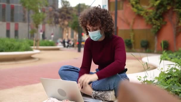 Ψυχωτική νεαρή επιχειρηματίας με μάσκα προσώπου που εργάζεται με φορητό υπολογιστή σε εξωτερικούς χώρους - Πλάνα, βίντεο