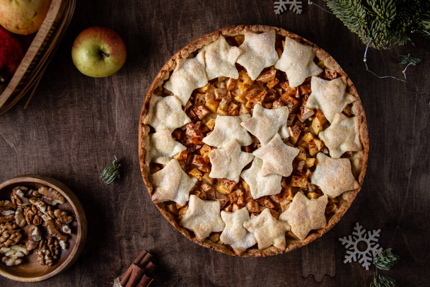Pie with apple, cinnamon and nuts on a brown wooden table, winter, top view, stars, snowflakes, fir branches, dark photo - Φωτογραφία, εικόνα