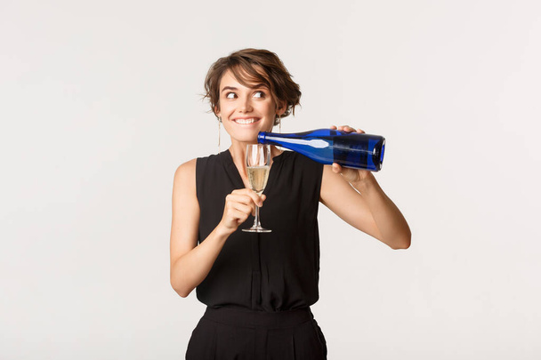 sluwe party meisje gieten zichzelf glas champagne en glimlachen opgewonden - Foto, afbeelding