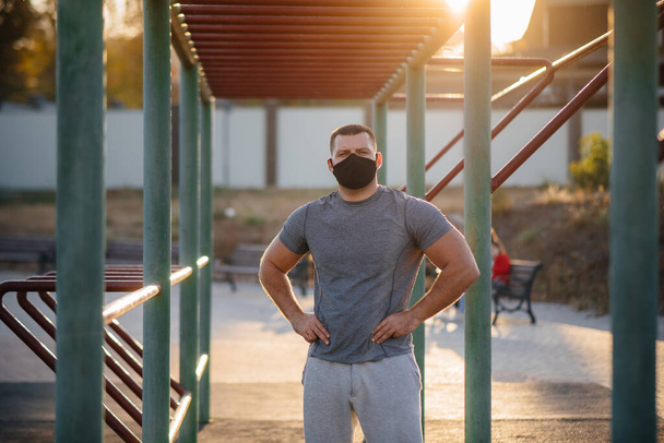 A young man does push-UPS, pull-UPS on a sports field in a mask during a pandemic at sunset. Sports, healthy lifestyle - Foto, Imagem