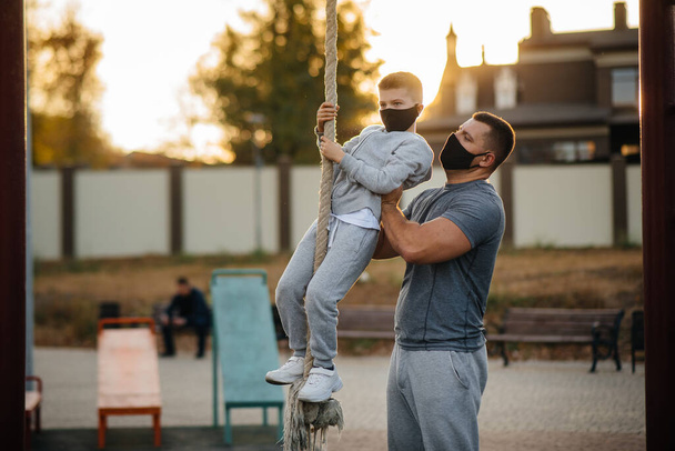 A father helps his son climb a rope on a sports field in masks during sunset. Healthy parenting and healthy lifestyle - Foto, Bild