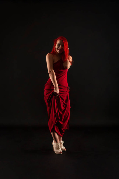 A girl with red hair, in a red dress posing on a dark background. Studio shooting . - Foto, Bild
