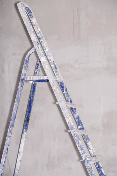 Single blue dirty aluminum folding metal step ladder leaning against grey plaster wall background. Vertical photo - Photo, Image