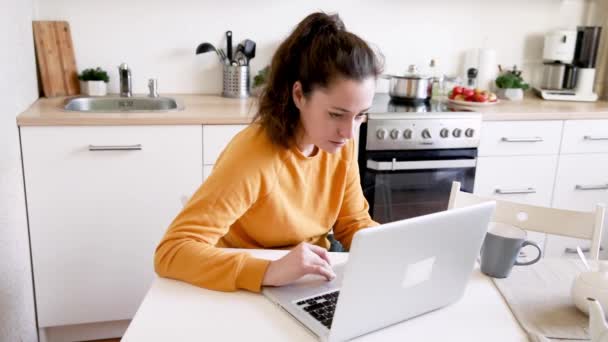Mobiles Büro zu Hause. Junge Frau, die zu Hause in der Küche sitzt und am Laptop arbeitet. Lifestyle-Mädchen studieren oder arbeiten in Innenräumen. Freiberufliches Quarantäne-Konzept - Filmmaterial, Video