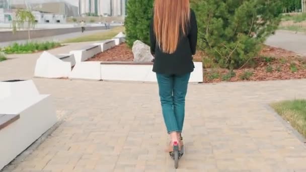 Seuranta back-view koko kuvan nuori pitkätukkainen nainen ratsastus sähkö skootteri ulkona puistossa - Materiaali, video